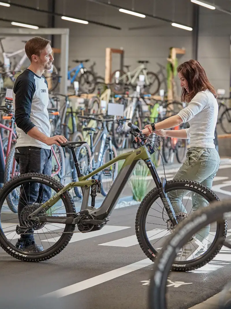 Eine Frau wird im Cube Store Chiemsee im Verkaufsraum kompetent zu einem E-Bike beraten.
