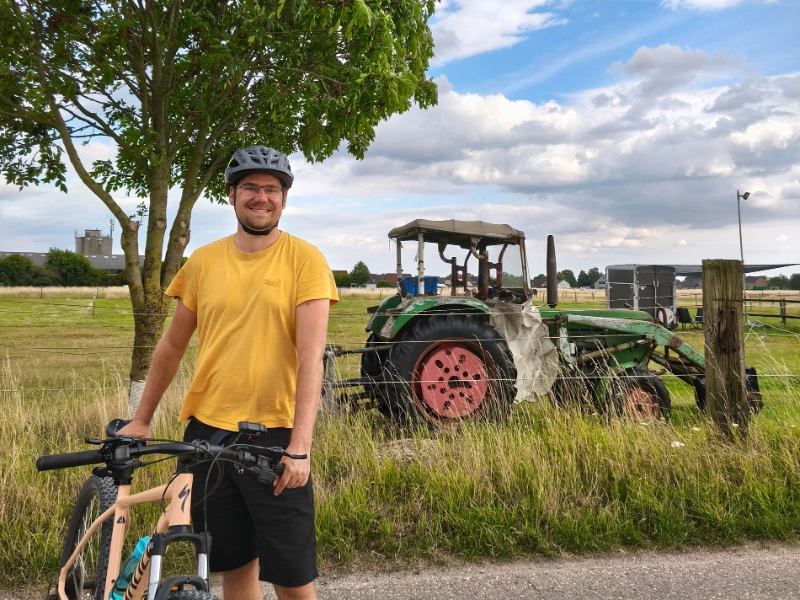 Sascha Düerkop steht mit seinem Fahrrad auf dem Feldweg, dahinter ein Traktor