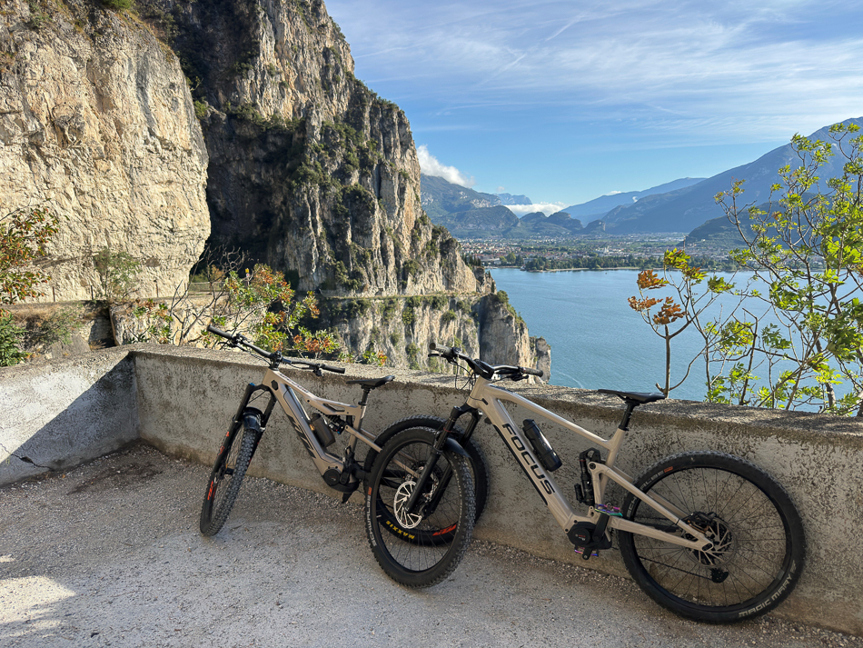 Zwei Mountainbikes stehen an einer Felswand mit Blick auf einen großen Bergsee und die umliegende Berglandschaft.