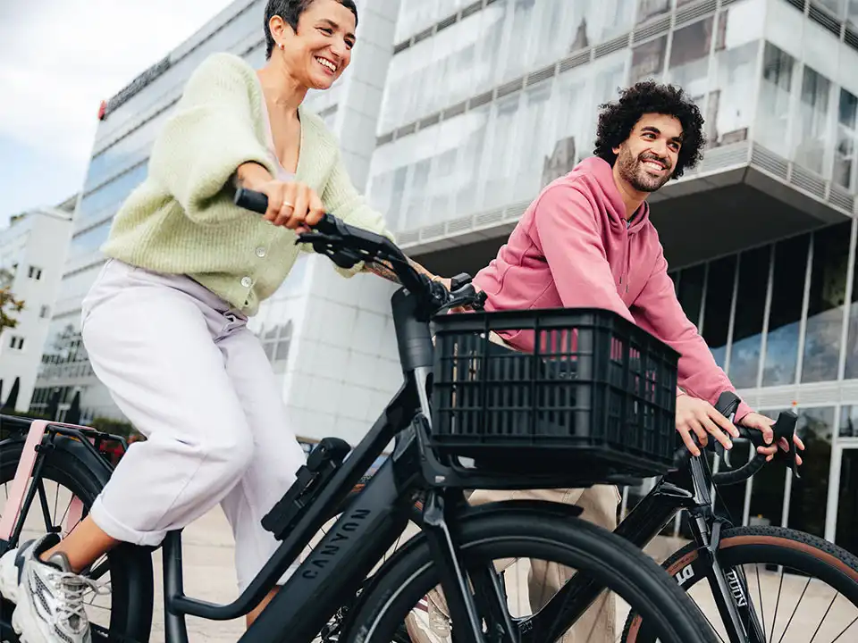 Mitarbeitende fahren lachend auf ihren Diensträdern an ihrem Bürogebäude vorbei