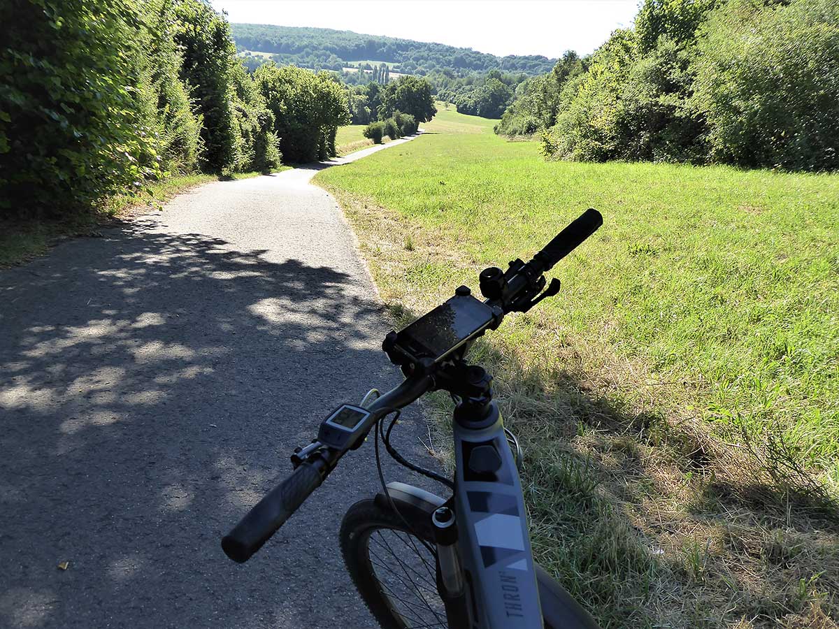 JobRad Moment von Roman: Blick über Fahrradlenker auf Feldweg, im Hintergrund Wiesen und Wälder