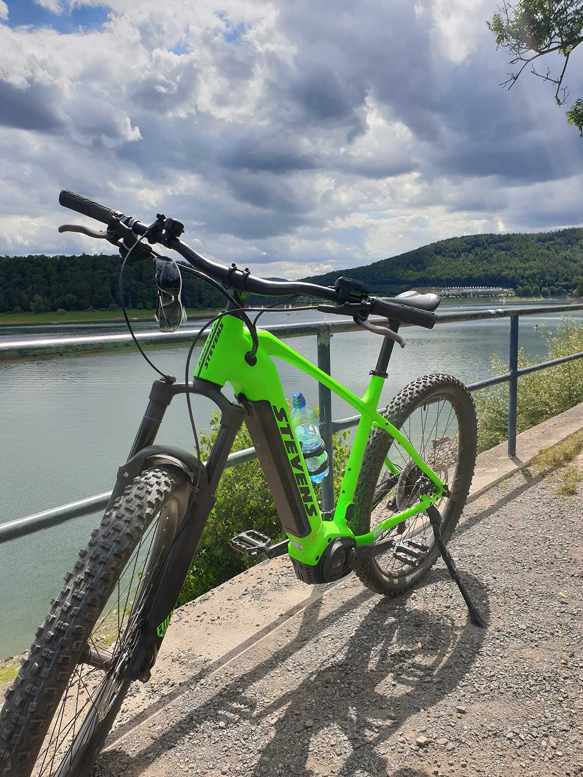 JobRad Moment von Aexander mit hellgrünem E-Mountainbike an Geländer vor See