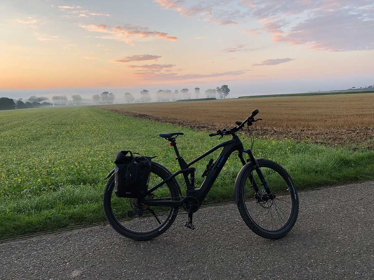 JobRad Moment von Robert: E-bike auf Feldweg, dahinter Wiese, Acker, Nebel, Morgenlicht