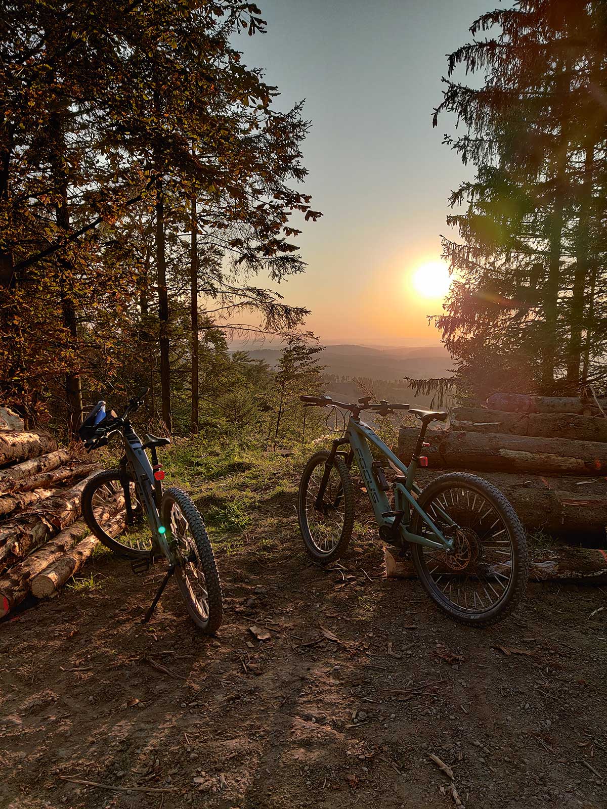 JobRad Moment von Daniel mit zwei Bikes auf Waldweg im Hintergrund dunstiger Sonnenuntergang und Aussicht
