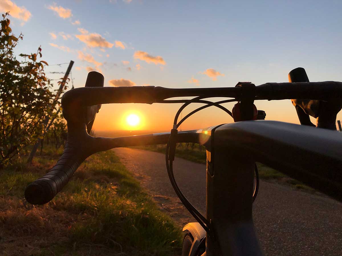 JobRad Moment von Martin, Blick über Rennradlenker über Feldweg zum Sonnenuntergang