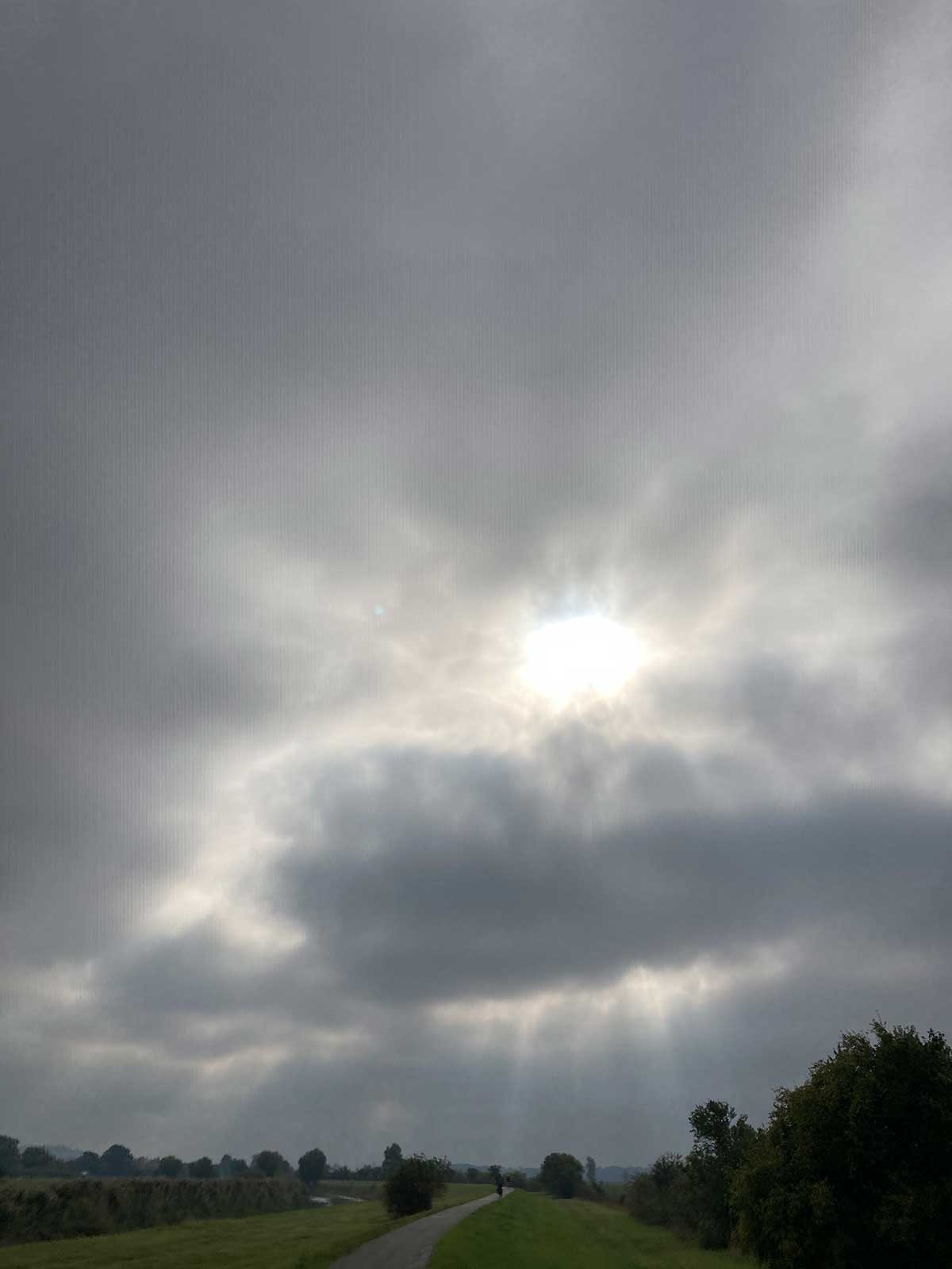 JObRad Moment von U. mit Blick auf Sonne hinter Wolken und Radweg im Grünen