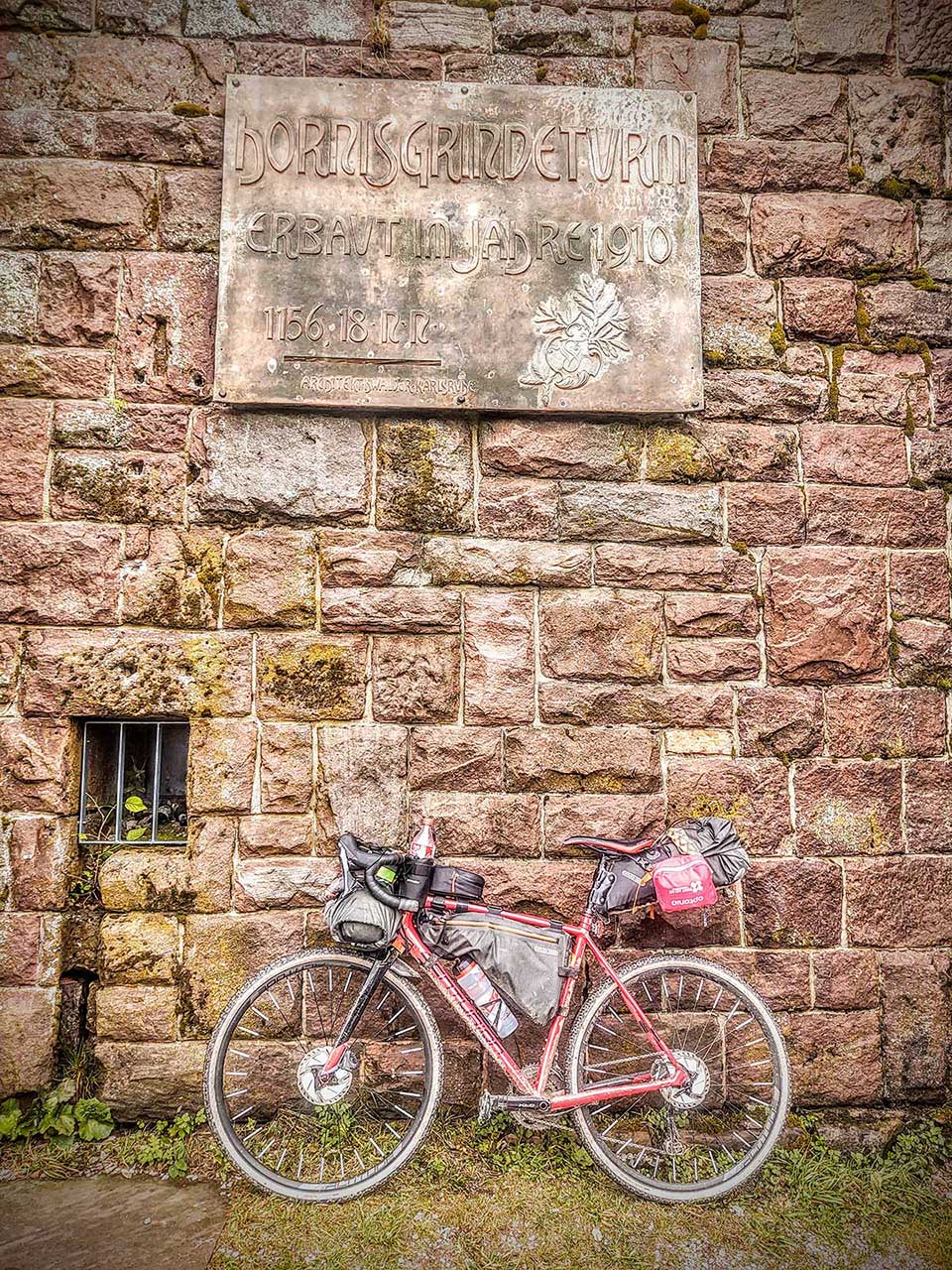 JobRad Moment von S. mit vollgepacktem Bike vor Steinquadermauer mit Plakette 