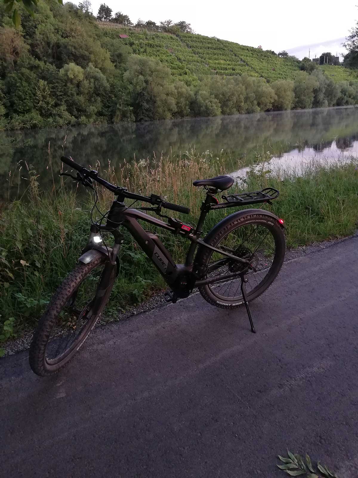 JobRad Moment von Heike mit Fahrrad auf Radweg am Fluss, am anderen Ufer Weinberge