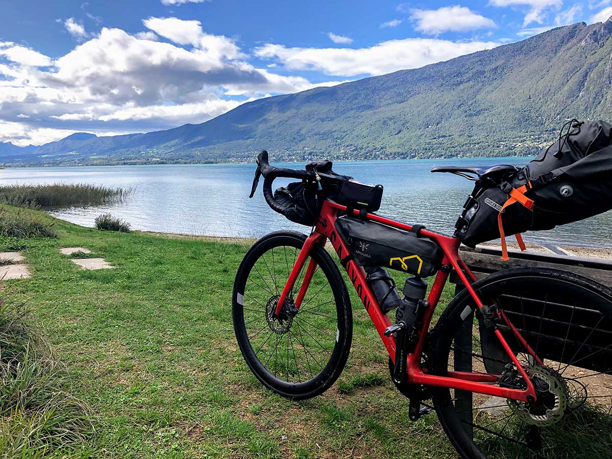 JobRad Moment von Stephane mit bepacktem rotem Bike an Bank vor See und Bergen