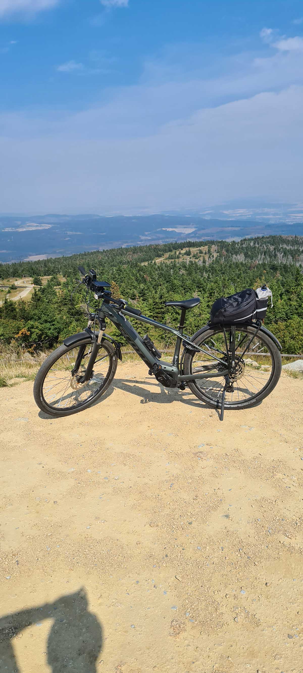 JobRad Moment von Heike mit grauem Fahrrad auf Anhöhe, im Hintergrund Aussicht auf Wälder und Ebene im Dunst